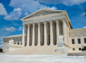 The supreme court of the united states with a blue, sky filled cloud behind it.