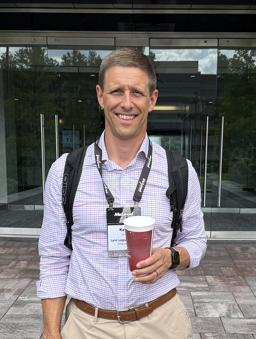 A man stands in front of glass doors with a backpack on, holding a coffee cup